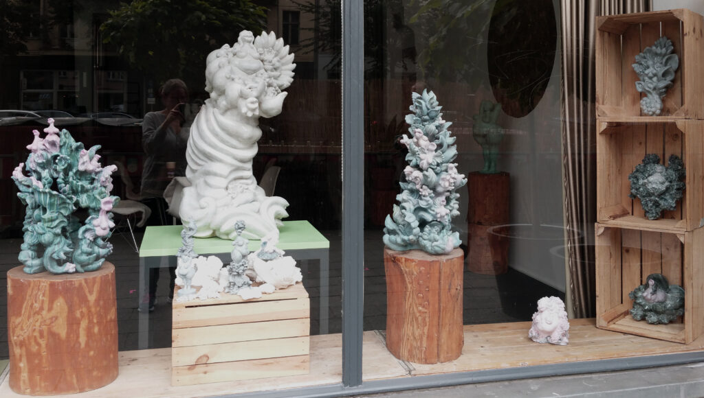 ceramics made of wildly growing plants, animals and baroque ornamental elements in blue-green-pink and white patina.exhibition view in the shop window